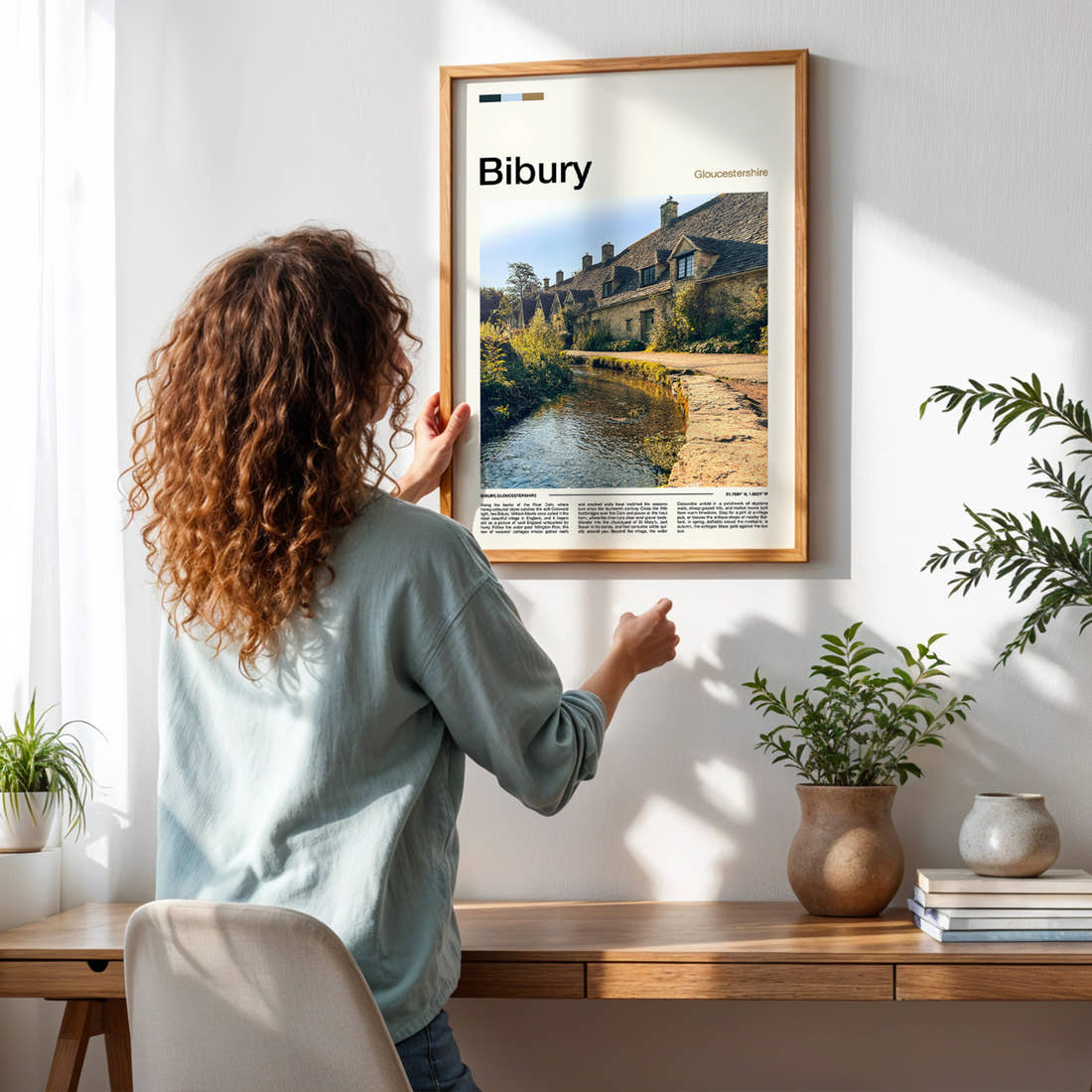 Bibury Riverside Cottage Row Travel Print framed on a pale wall beside houseplants