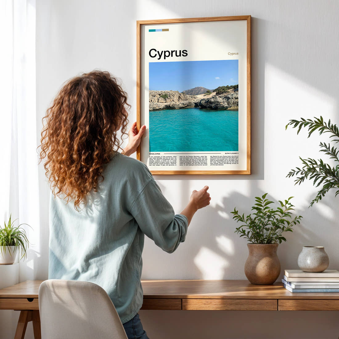 Cyprus Turquoise Rocky Cove Travel Print framed on a pale wall beside houseplants