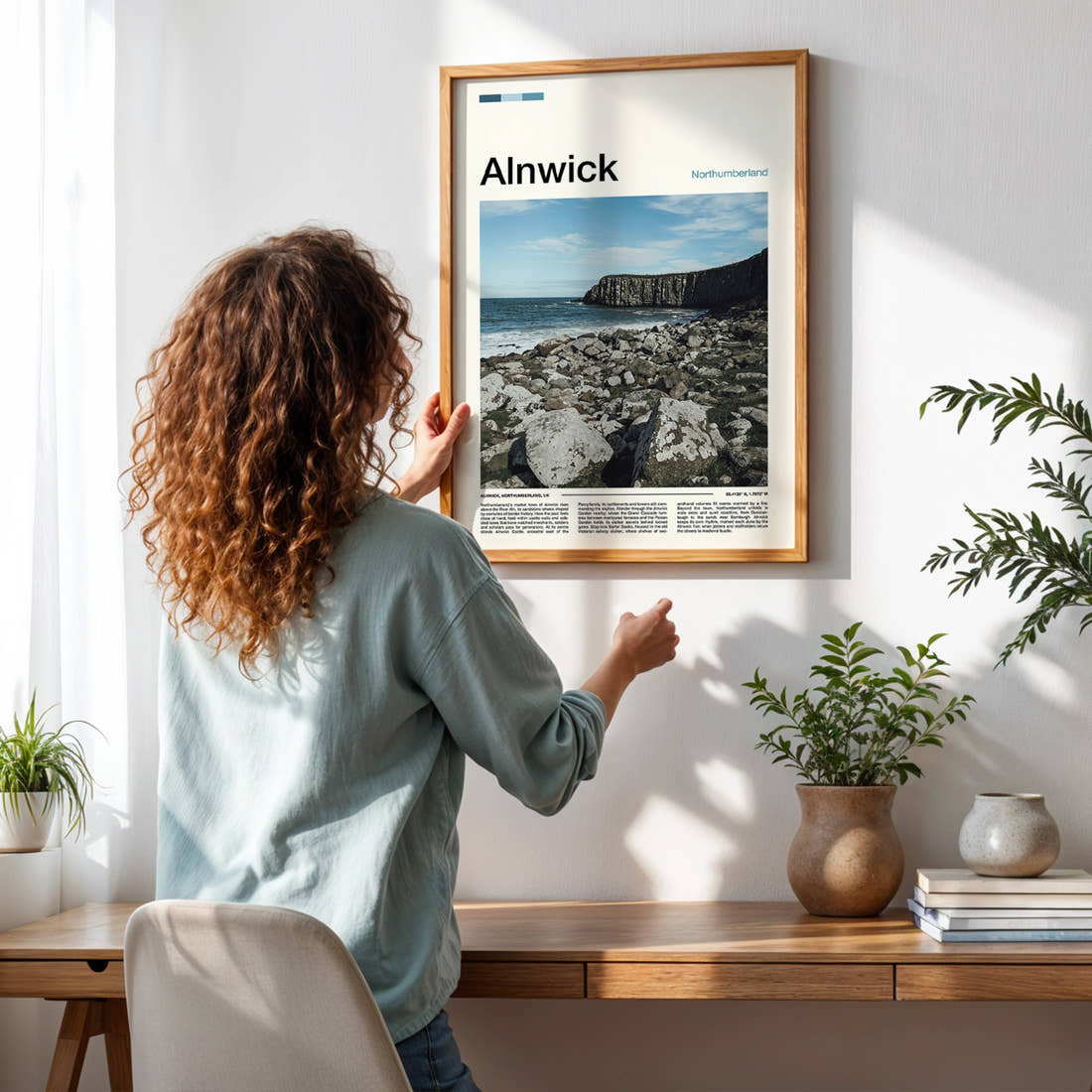 Alnwick Rocky Coastal Cliffs Travel Print framed on a pale wall beside houseplants