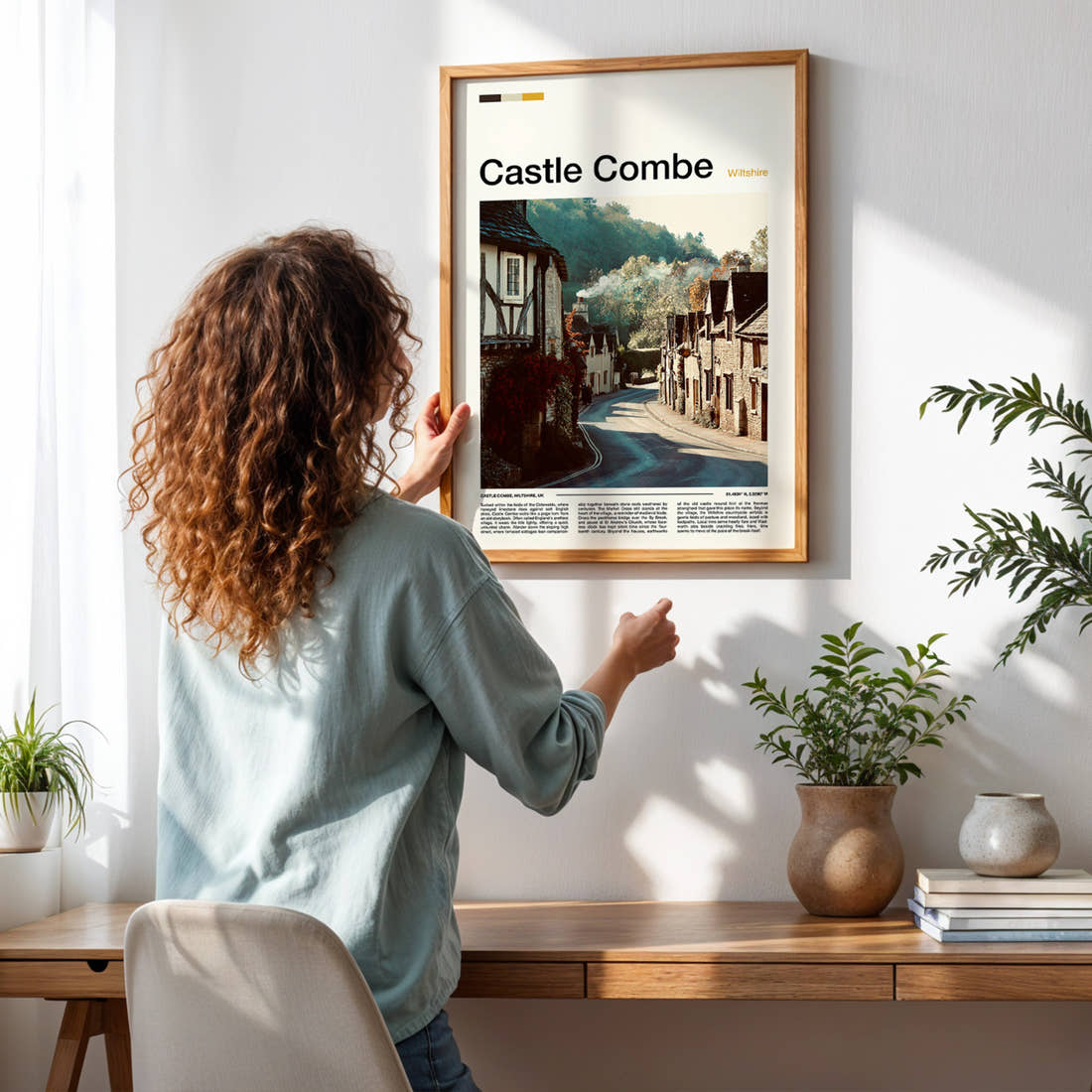 Castle Combe Honey-Stone Village Lane Travel Print framed on a pale wall beside houseplants
